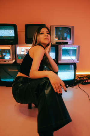Portrait of young attractive caucasian woman in stylish outfit posing near stand with retro tvs.