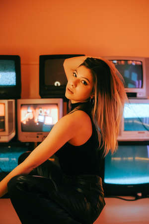 Portrait of young attractive caucasian woman in stylish outfit posing near stand with retro tvs.の写真素材