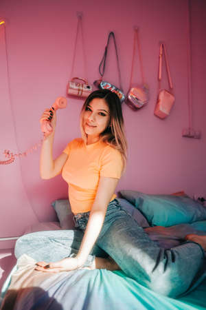 Portrait of young attractive cheerful woman sitting in a bedroom with pink walls.の写真素材