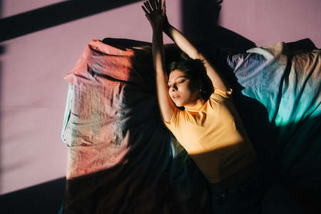 Young attractive caucasian woman relaxing on a bed in sunlight.の写真素材