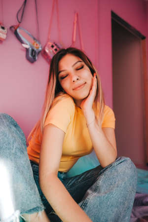 Portrait of young attractive cheerful woman sitting in a bedroom with pink walls.の写真素材