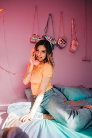 Portrait of young attractive cheerful woman sitting in a bedroom with pink walls.の写真素材