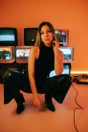 Portrait of young attractive caucasian woman in stylish outfit posing near stand with retro tvs.の写真素材