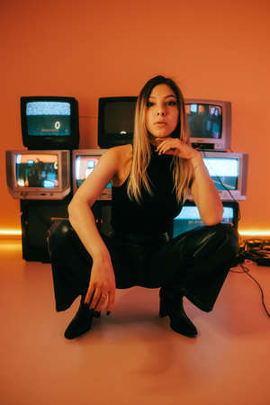 Portrait of young attractive caucasian woman in stylish outfit posing near stand with retro tvs.の写真素材