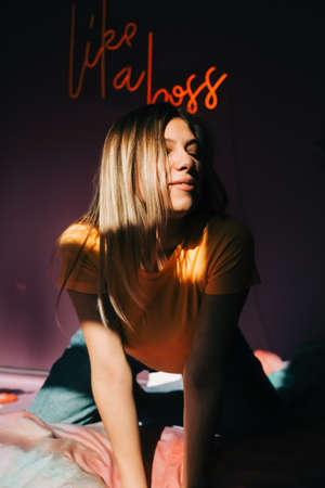 Portrait of young attractive caucasian woman posing in a bedroom in sunlight.
