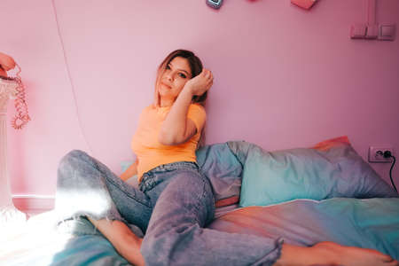Portrait of young attractive cheerful woman sitting in a bedroom with pink walls.の写真素材