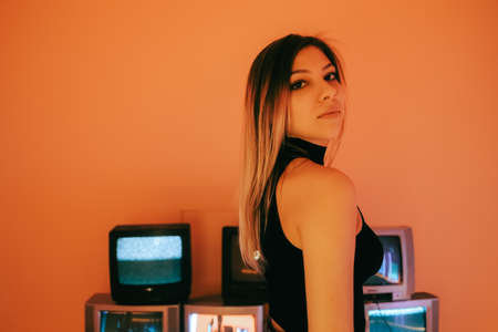 Portrait of young attractive caucasian woman in stylish outfit posing near stand with retro tvs.の写真素材