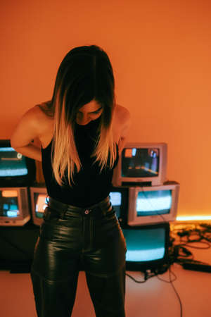 Portrait of young attractive caucasian woman in stylish outfit posing near stand with retro tvs.の写真素材