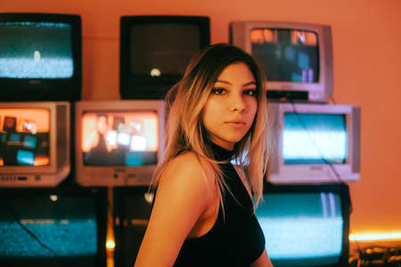 Portrait of young attractive caucasian woman in stylish outfit posing near stand with retro tvs.の写真素材