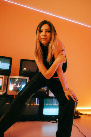 Portrait of young attractive caucasian woman in stylish outfit posing near stand with retro tvs.の写真素材