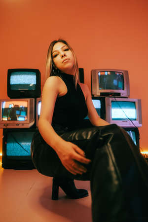 Portrait of young attractive caucasian woman in stylish outfit posing near stand with retro tvs.の写真素材