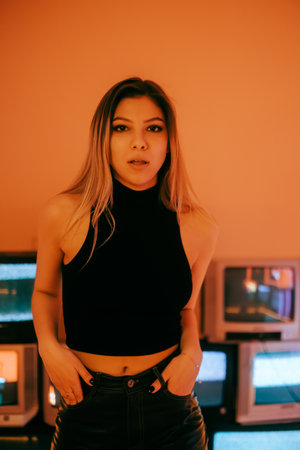 Portrait of young attractive caucasian woman in stylish outfit posing near stand with retro tvs.の写真素材