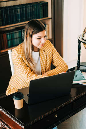 Portrait of young woman college student using mobile phone, preparing for test exam, writing essay doing homework in the library.の写真素材