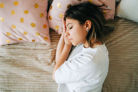 Young caucasian woman lying on a bed, sleeping after hard-working day, tired millennial female fall asleep in bedroom at home, take nap or daydream, fatigue conceptの写真素材