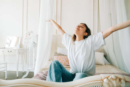 Attractive caucasian young woman in doing stretching exercise sitting on a bed and enjoying sunny morning.の写真素材