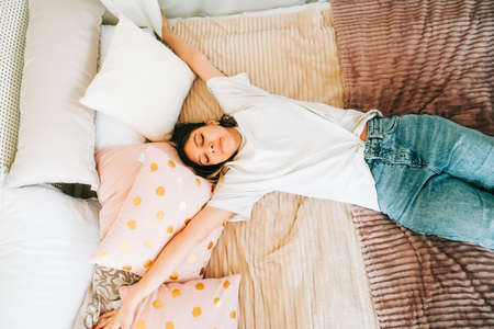 Attractive caucasian young woman is doing stretching exercise lying on a bed and enjoying sunny morning.の写真素材