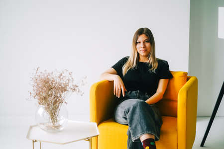 Portrait of attractive caucasian woman sitting on armchair at home and looking on camera.の写真素材