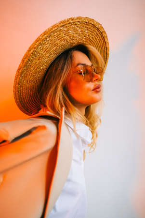 Portrait of attractive caucasian woman in eyeglasses and wicker hat wearing in stylish outfit, posing on white wall background.の写真素材