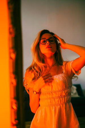 Young attractive woman looking on herself in the mirror in the evening in orange light.の写真素材