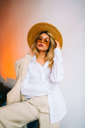 Portrait of attractive caucasian woman in eyeglasses and wicker hat wearing in stylish outfit, posing on white wall background.の写真素材