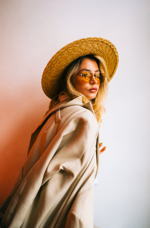 Portrait of attractive caucasian woman in eyeglasses and wicker hat wearing in stylish outfit, posing on white wall background.の写真素材