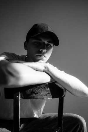 Portrait of handsome caucasian man fashion model in t shirt and cap sitting on chair, studio shot.の写真素材