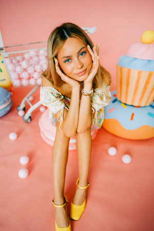 Portrait of attractive caucasian woman fashion model with blond hair, on pink background with figures of sweets and candies.の写真素材