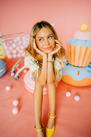 Portrait of attractive caucasian woman fashion model with blond hair, on pink background with figures of sweets and candies.の写真素材