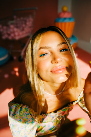 Portrait of attractive caucasian woman fashion model with blond hair, on pink background with figures of sweets and candies.の写真素材