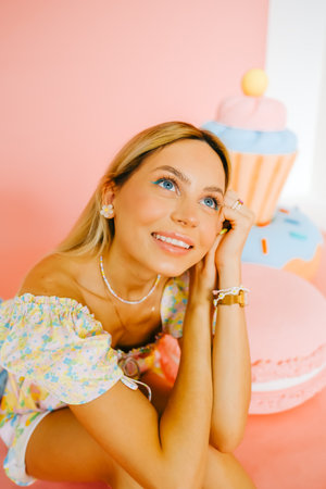Portrait of attractive caucasian woman fashion model with blond hair, on pink background with figures of sweets and candies.の写真素材