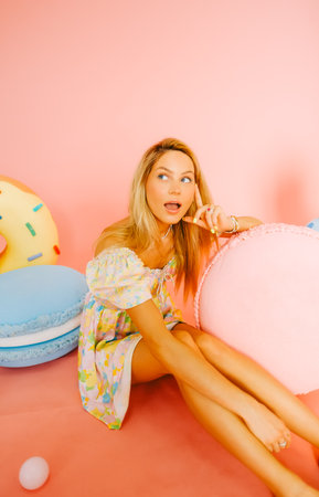 Portrait of attractive caucasian woman fashion model with blond hair, on pink background with figures of sweets and candies.の写真素材