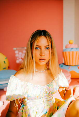 Portrait of attractive caucasian woman fashion model with blond hair, on pink background with figures of sweets and candies.の写真素材