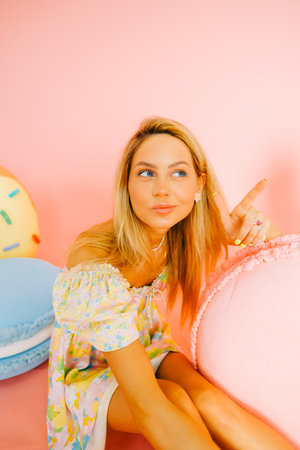 Portrait of attractive caucasian woman fashion model with blond hair, on pink background with figures of sweets and candies.の写真素材