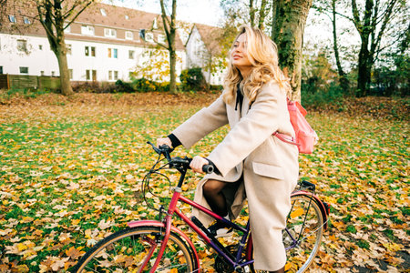 Young attractive caucasian woman ride on bicycle in the park on warm day in the fall.の写真素材