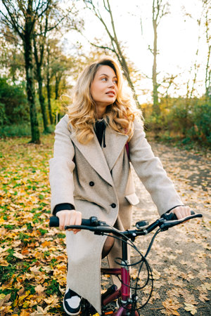 Young attractive caucasian woman ride on bicycle in the park on warm day in the fall.の写真素材
