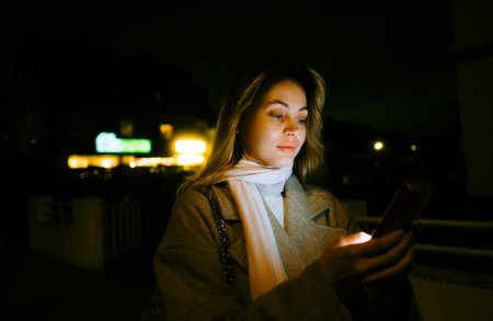 Young caucasian woman using mobile phone outdoor in the evening, walking on city streets.の写真素材