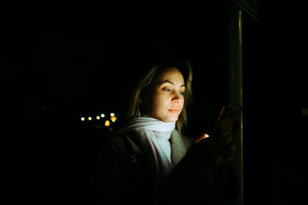 Young caucasian woman using mobile phone outdoor in the evening, walking on city streets.の写真素材