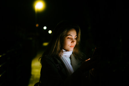 Young caucasian woman using mobile phone outdoor in the evening, walking on city streets.の写真素材