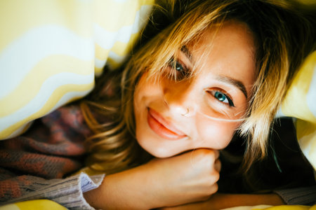 Portrait of happy attractive caucasian woman lying under the blanket at home, comfort feelingの写真素材