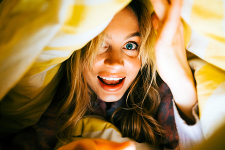 Portrait of cheerful attractive caucasian woman lying under the blanket at home and having fun, home comfort feelingの写真素材