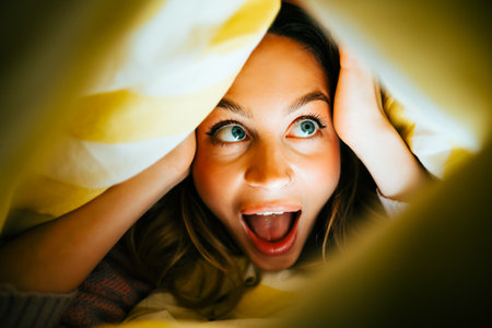 Portrait of cheerful attractive caucasian woman lying under the blanket at home and having fun, home comfort feelingの写真素材