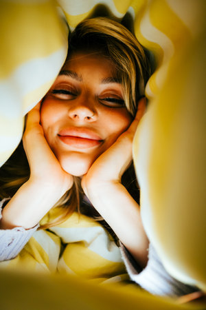 Portrait of happy attractive caucasian woman lying under the blanket at home, comfort feelingの写真素材