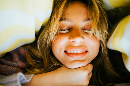 Portrait of happy attractive caucasian woman lying under the blanket at home, comfort feelingの写真素材