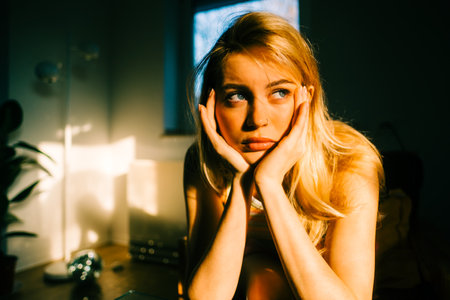 Young bored millennial woman sitting on a sofa alone at home. Fatigue or emotionally exhausted conceptの写真素材