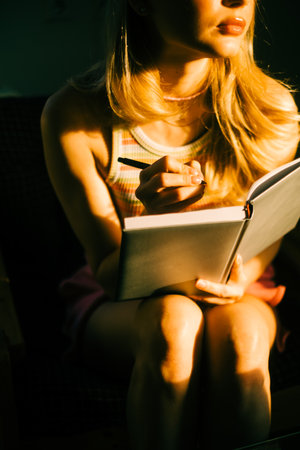 Caucasian woman making notes at home in sunset light.の写真素材