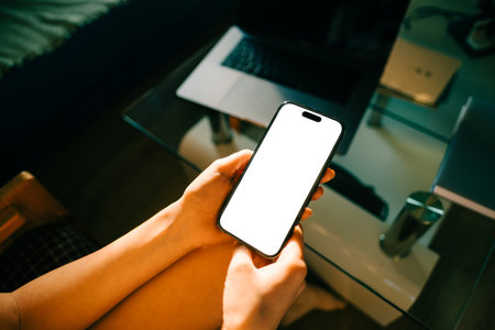 Woman holding mobile phone with white screen mock up, resting on a sofa in living room at home.の写真素材