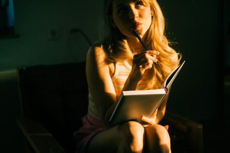 Caucasian woman making notes at home in sunset light.の写真素材