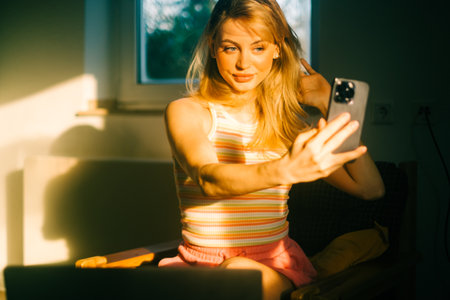 Young caucasian woman using mobile phone at home, making selfie photo.の写真素材