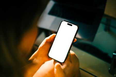 Woman holding mobile phone with white screen mock up, resting on a sofa in living room at home.の写真素材