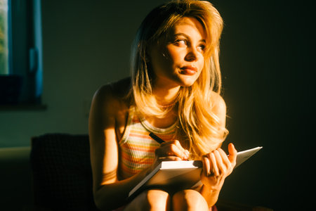 Caucasian woman making notes at home in sunset light.の写真素材